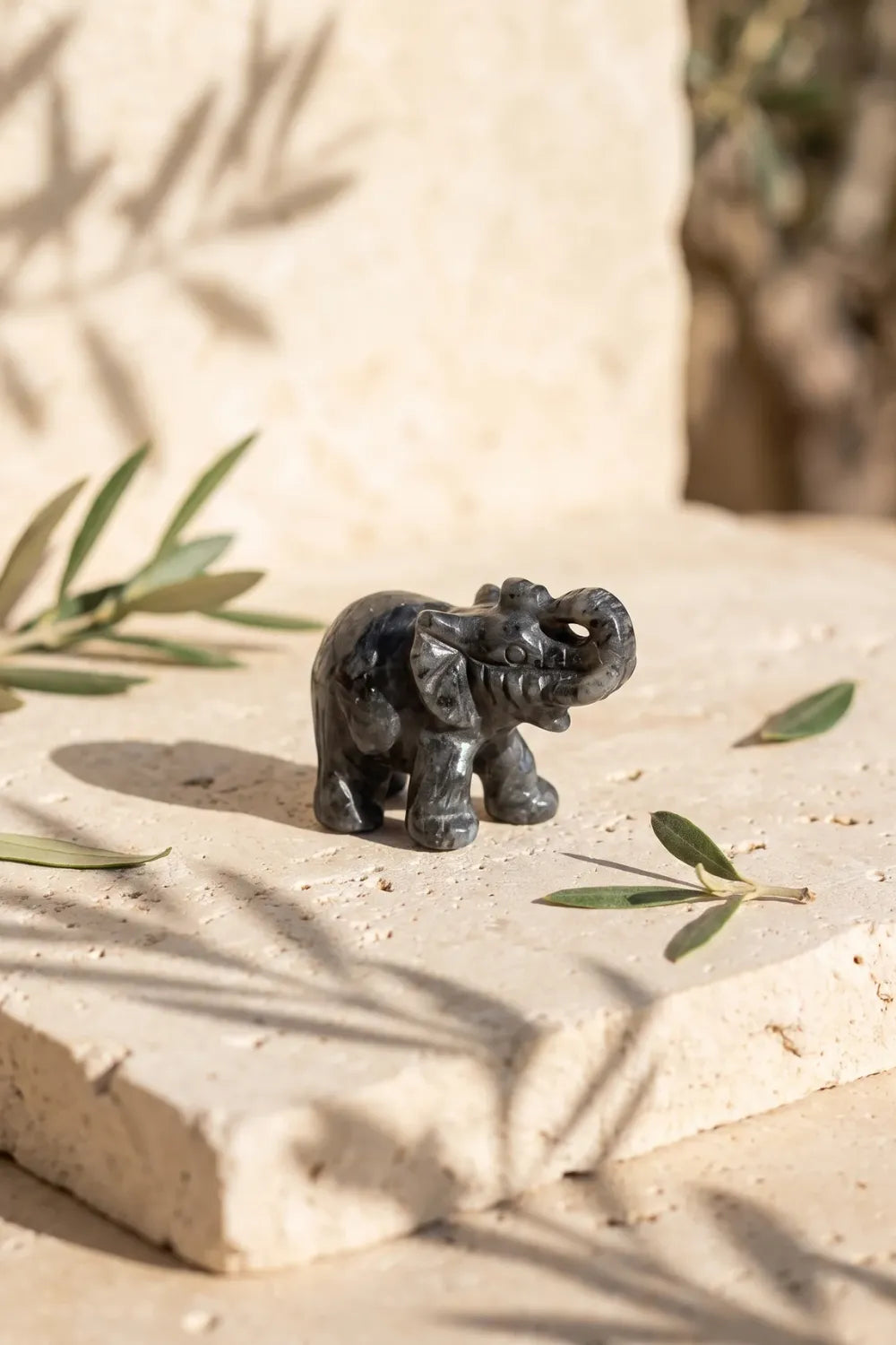 Elefante de la suerte tallado en labradorita sobre una piedra de travertino en un jardín - Anna Piedra