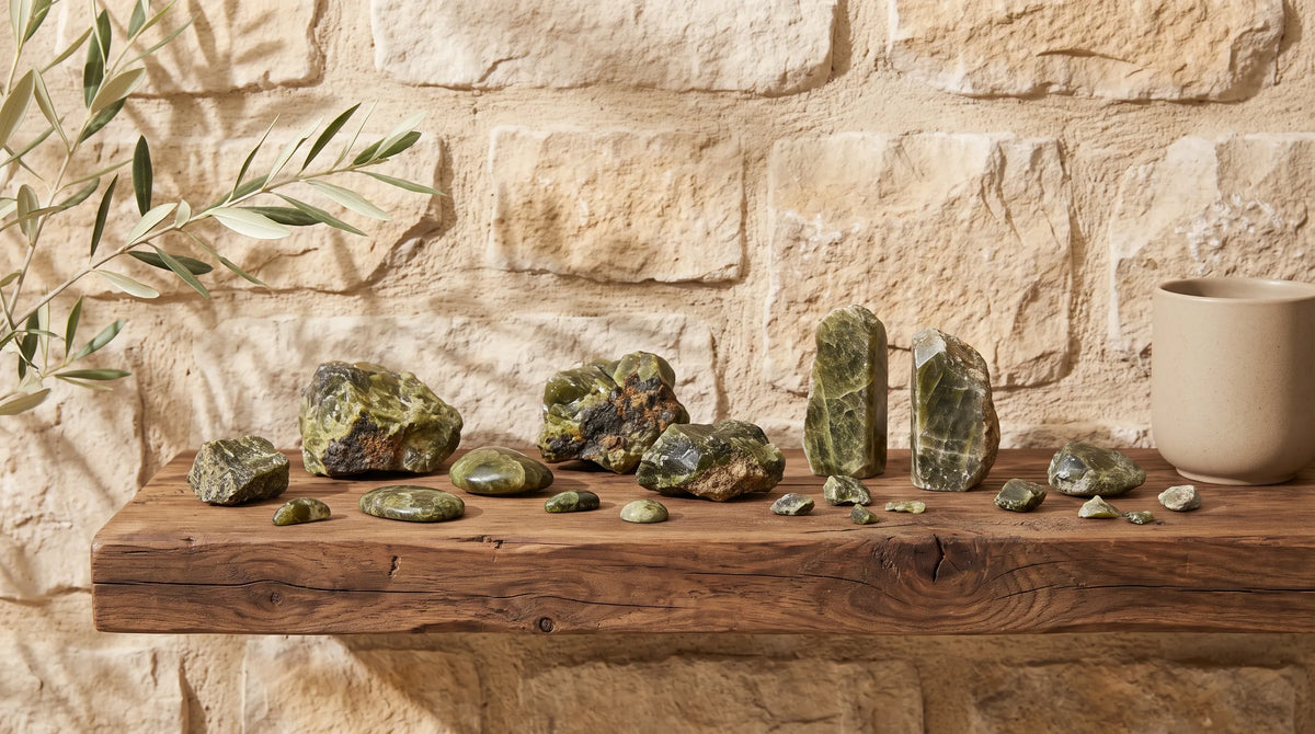 Colección de epidota natural en distintas formas y tamaños sobre una estantería  de madera frente a una pared de piedra. anna piedra