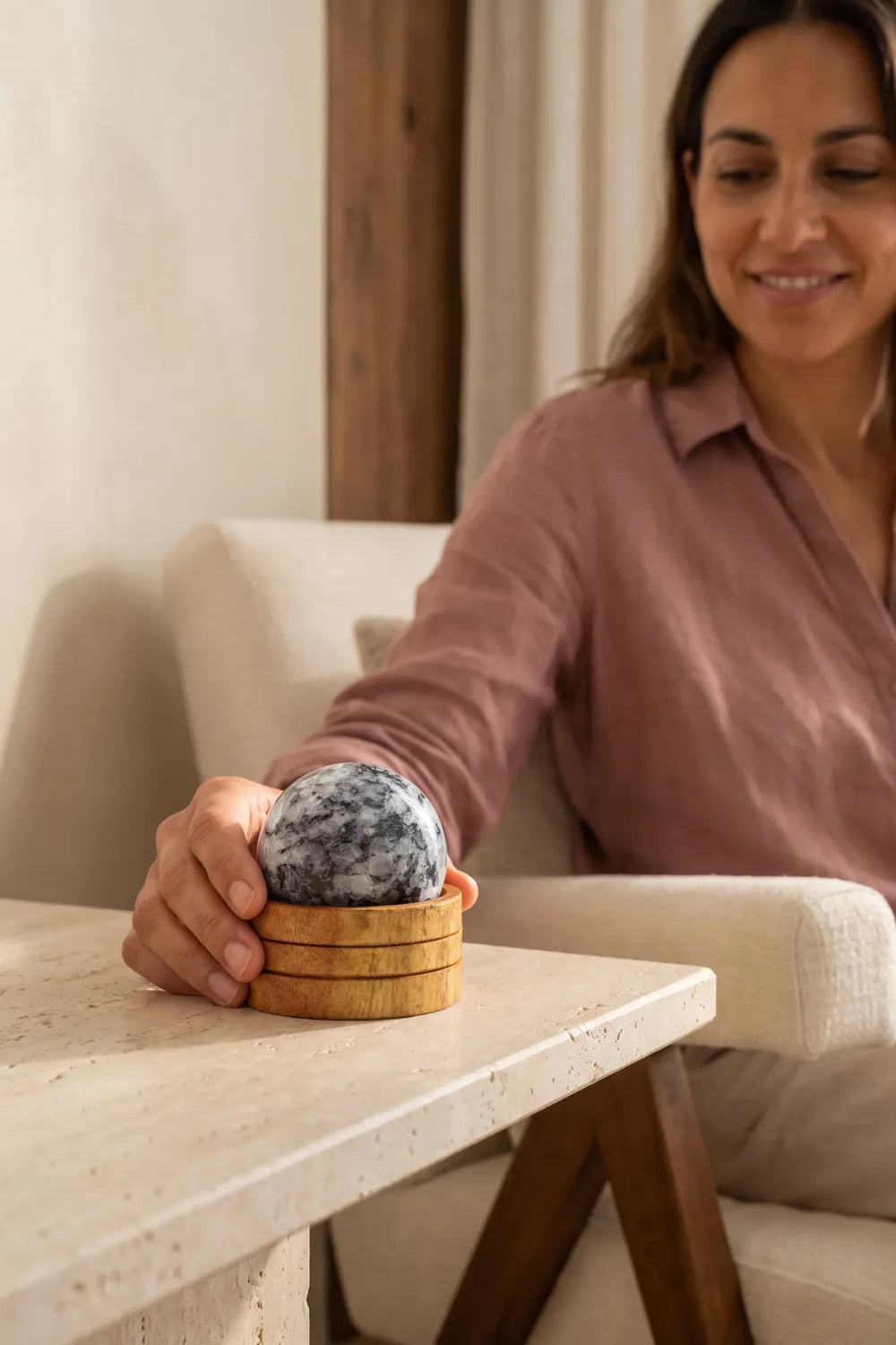 Mujer colocando una esfera de piedra luna blanca y negra sobre una base de madera en una mesa de piedra clara – Anna Piedra