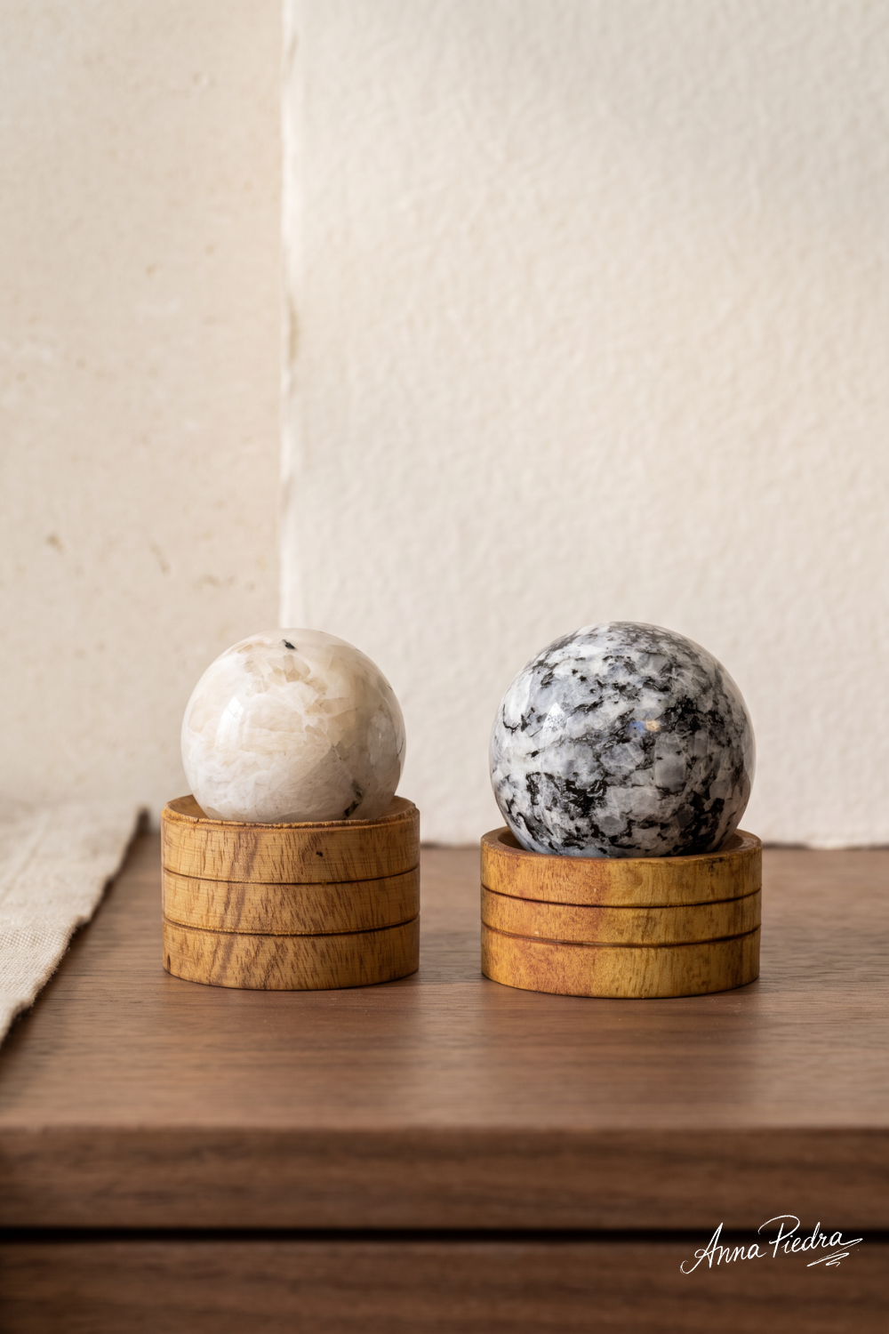 Esferas de piedra luna natural pulidas en dos tamaños, una blanca y otra con vetas negras, sobre soportes redondos de madera – Anna Piedra