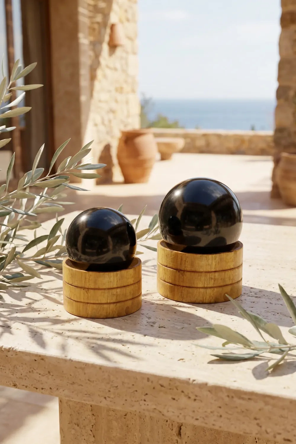 Dos esferas de turmalina negra 40 mm y 50 mm sobre soportes de madera en terraza con vista al mar - Anna Piedra