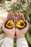 Dos mitades de una geoda de calcita amarilla sostenidas en las manos en un jardín mediterráneo. anna piedra