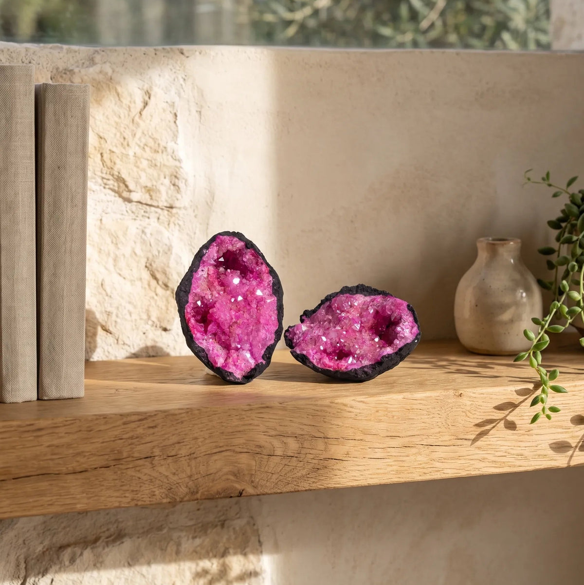 Geoda de calcita rosa abierta en dos mitades sobre una estantería de madera en un interior mediterráneo lumineux. anna piedra 
