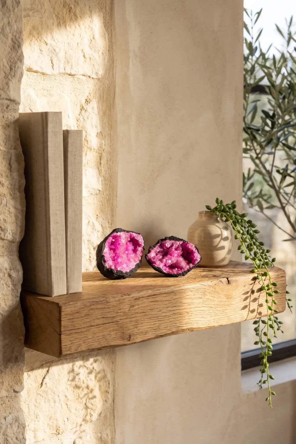 Geoda de calcita rosa abierta en dos mitades sobre una estantería de madera en un interior mediterráneo. anna piedra