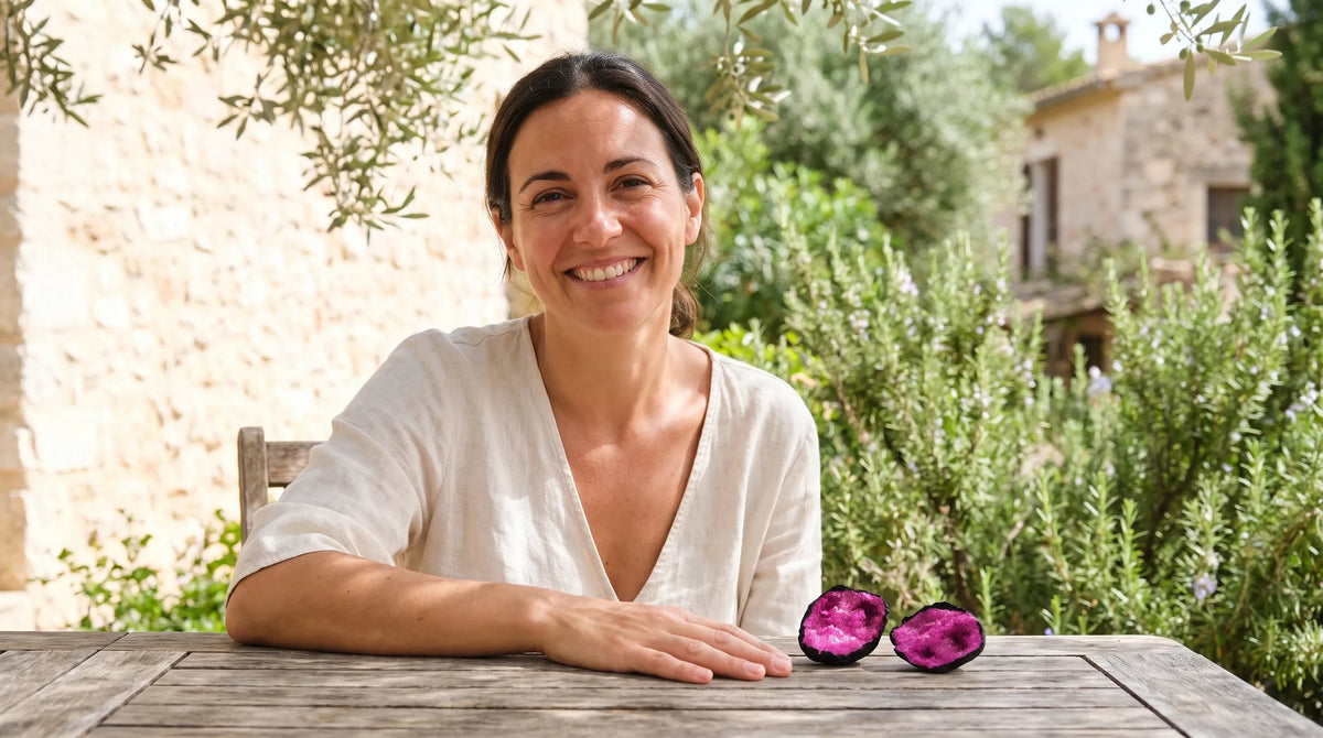 Geoda de calcita rosa abierta en dos mitades sobre una mesa de madera, junto a una mujer en un jardín mediterráneo. anna piedra