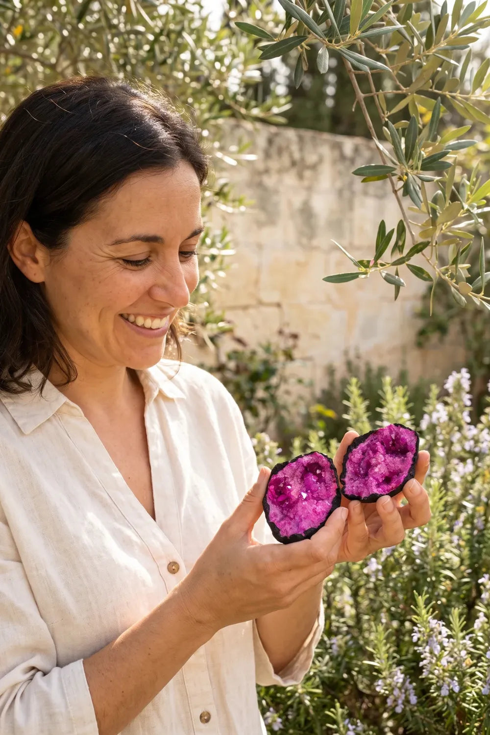 Mujer sosteniendo una geoda de calcita rosa abierta en dos mitades en un jardín mediterráneo. anna piedra