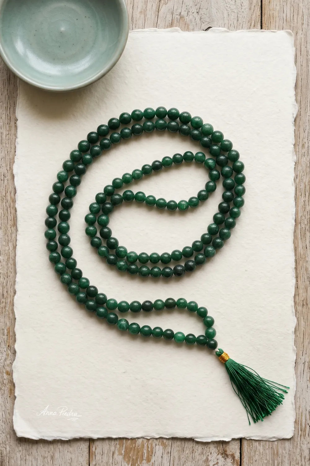 Vista superior de un japamala de 108 cuentas de jade verde dispuesto sobre papel artesanal claro, con borla verde.