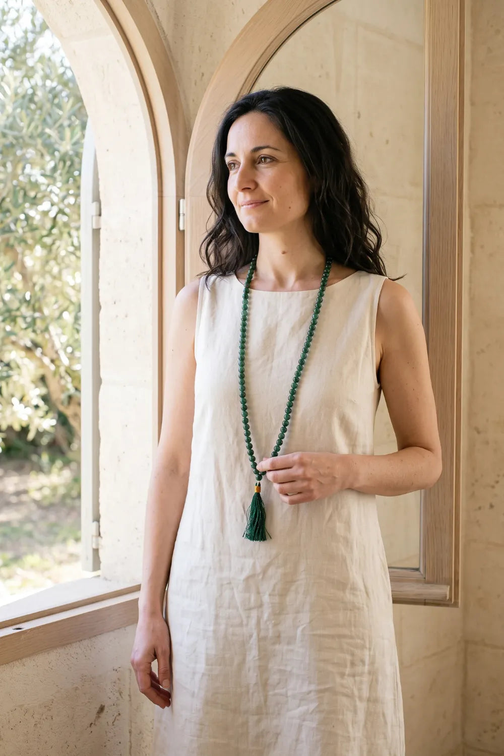 Mujer con vestido de lino blanco luciendo un japamala largo de jade verde de 108 cuentas con borla verde.