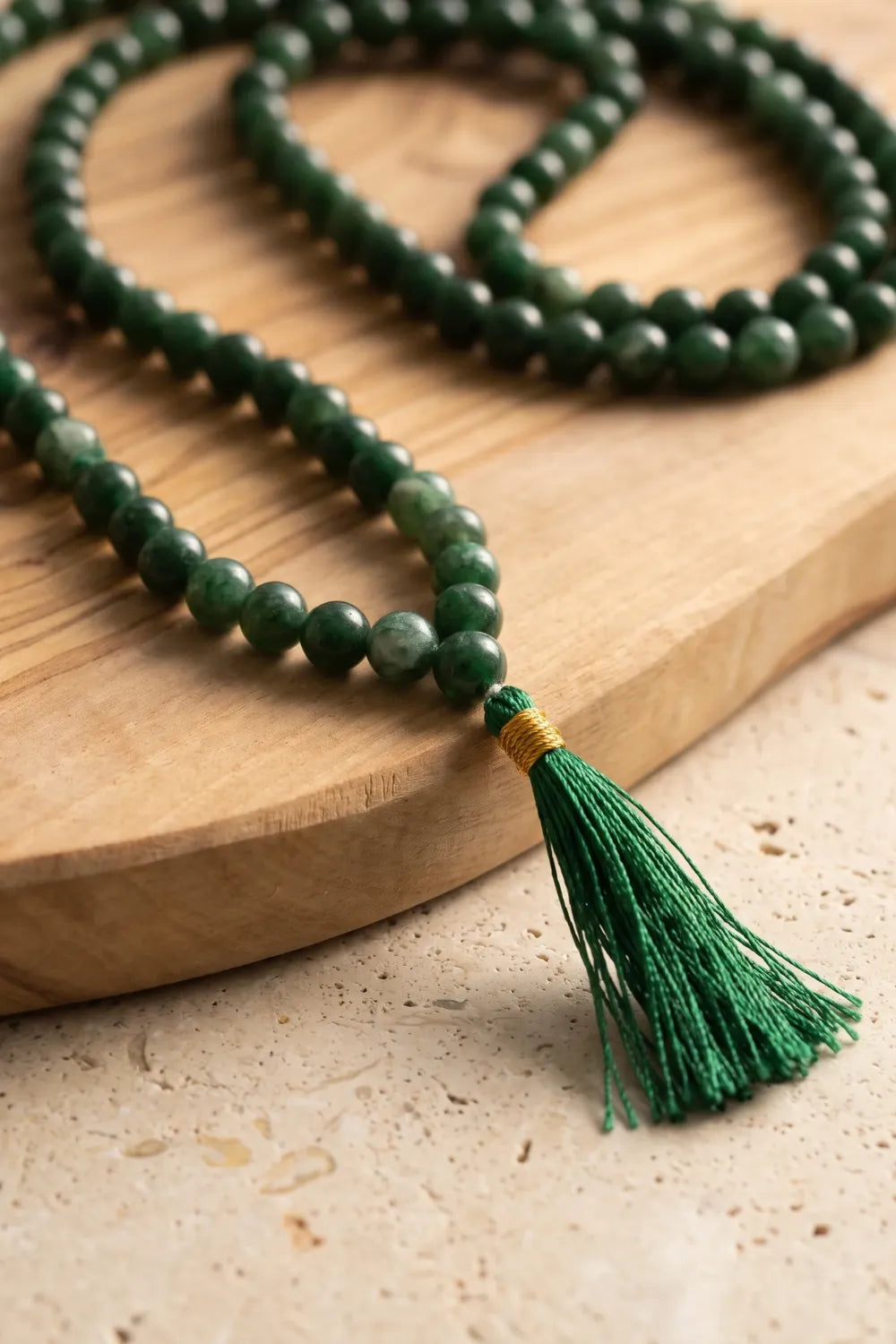 Primer plano de las cuentas redondas de jade verde y la borla de hilo verde con detalle dorado del japamala.