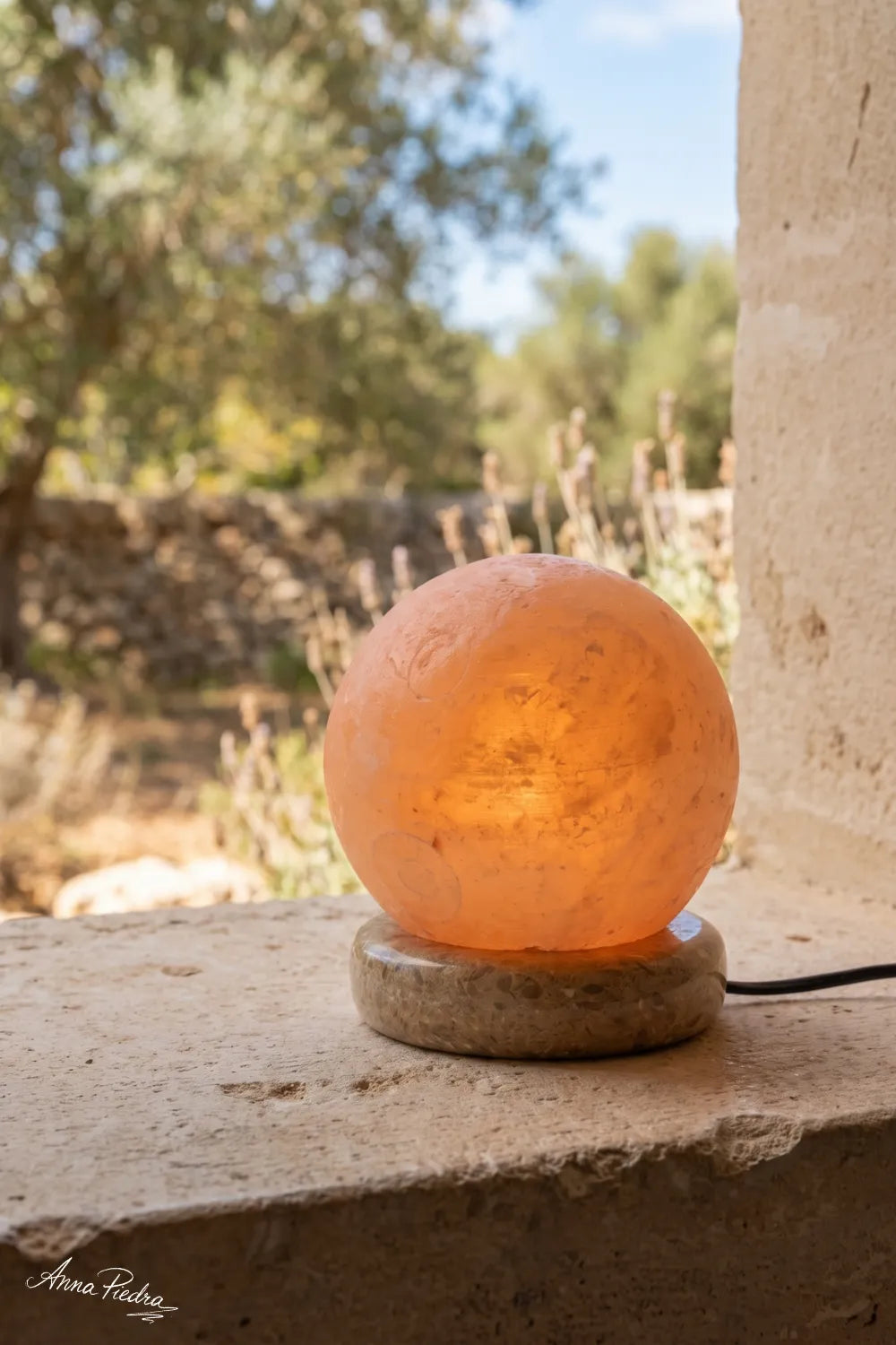 Lámpara de sal bola del Himalaya encendida junto a una ventana con vistas al exterior anna piedra