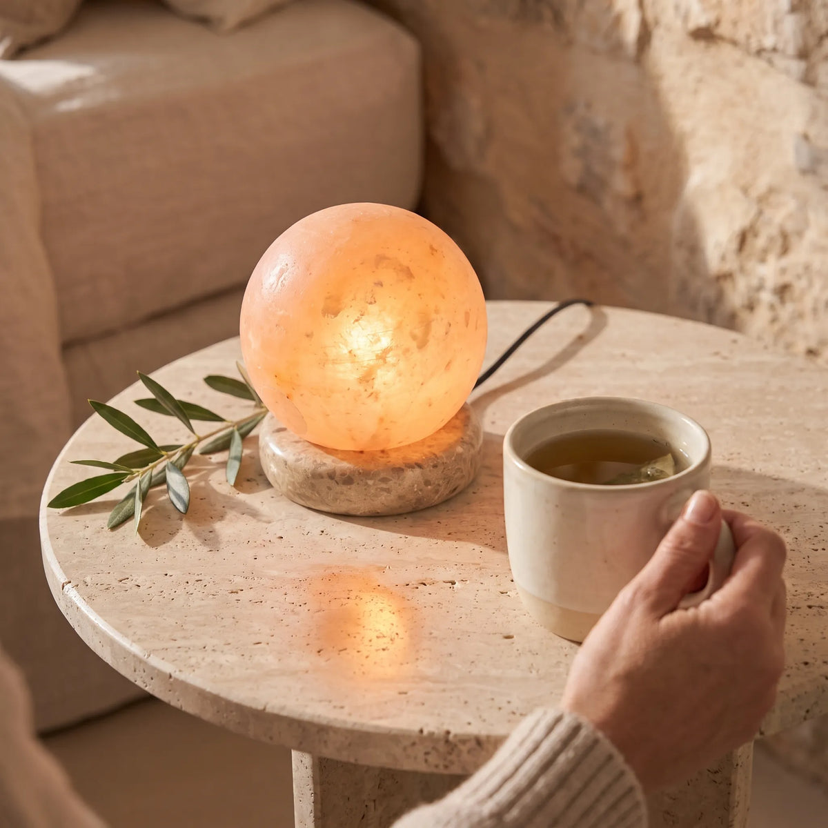 Lámpara de sal bola del Himalaya encendida sobre una mesa junto a una taza de té anna piedra