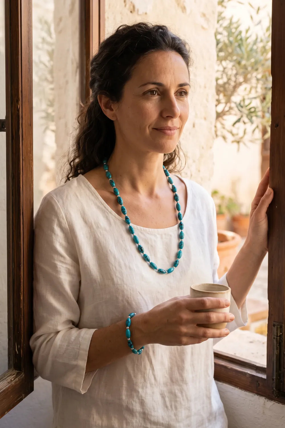 Mujer luciendo collar y pulsera de turquesa nepalí en un interior mediterráneo