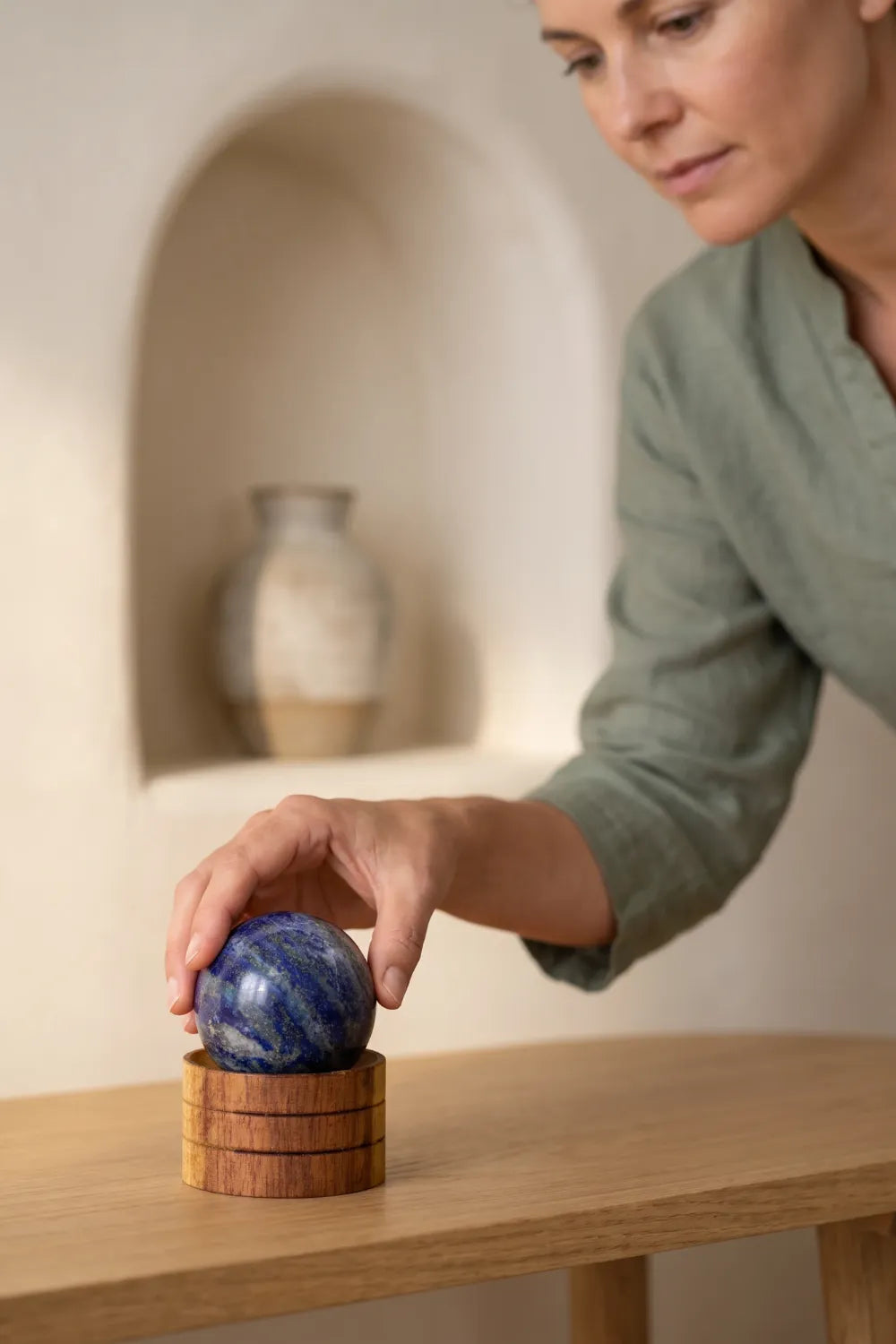 Mujer colocando una esfera de lapislázuli sobre una base de madera en una mesa de madera clara