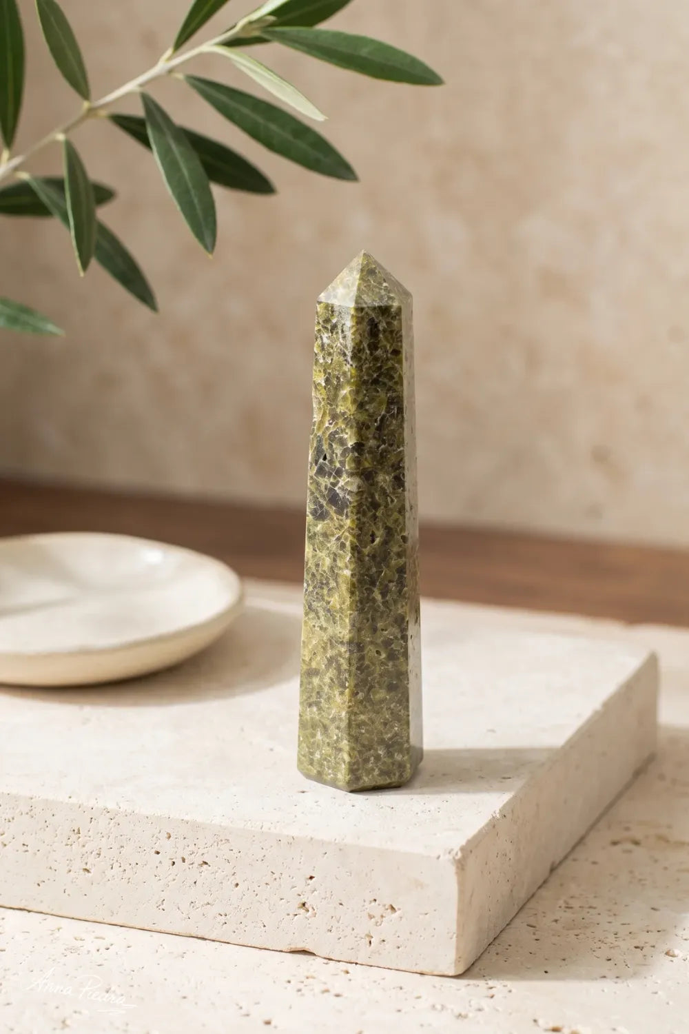 Detalle de un obelisco de epidota de seis caras sobre una superficie de piedra clara.