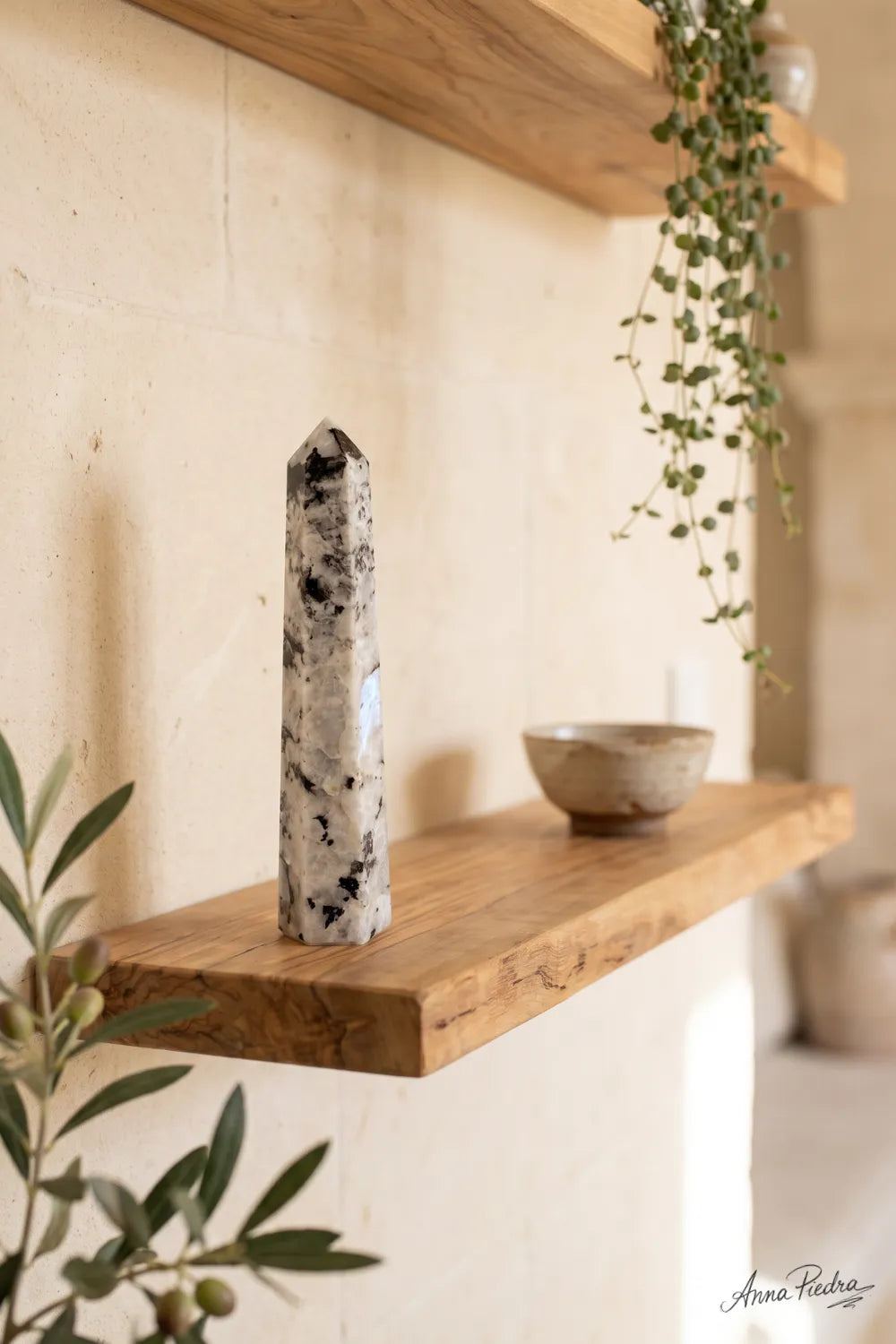Obelisco de piedra luna arcoíris de seis caras expuesto sobre una estantería de madera con decoración natural