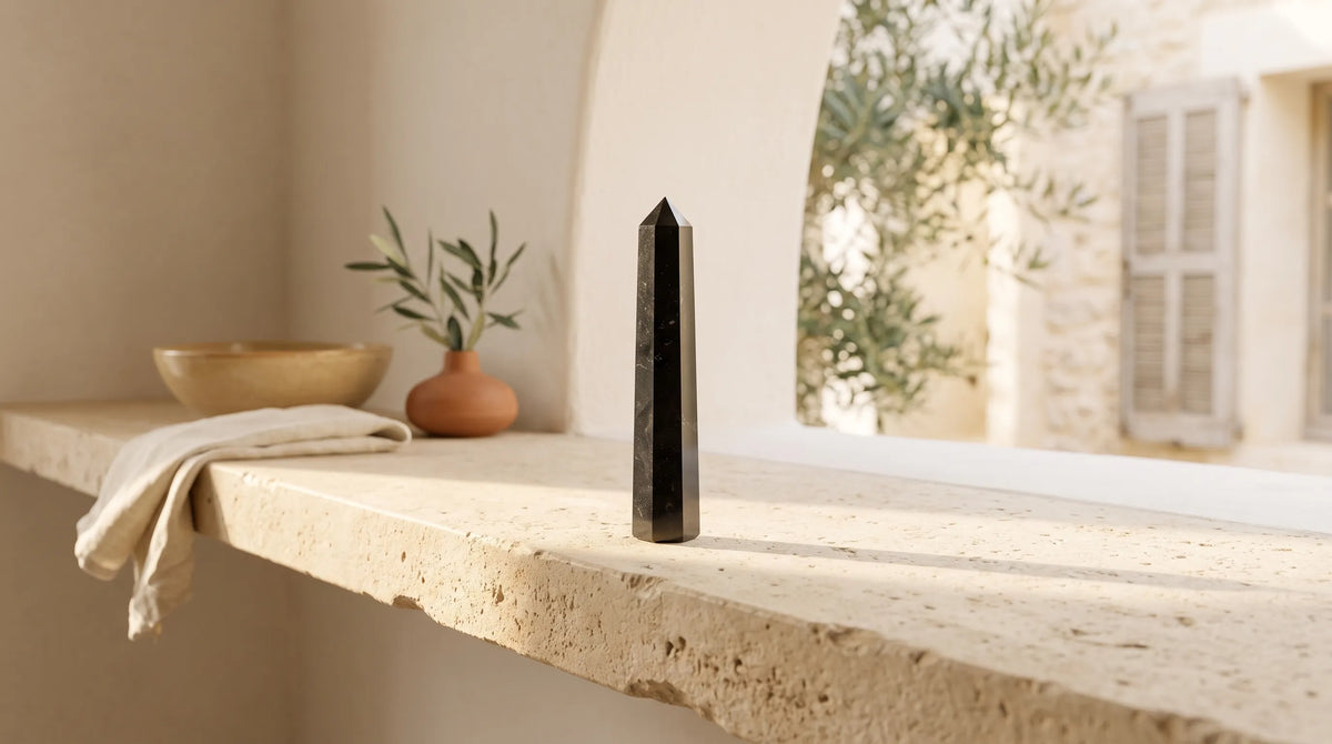Obelisco de turmalina negra colocado sobre una repisa de piedra en un interior cálido y luminoso de estilo mediterráneo.