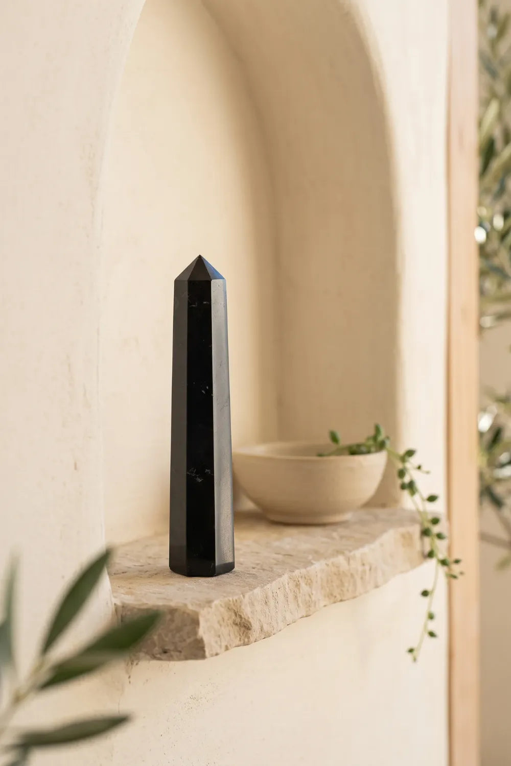 Obelisco de turmalina negra sobre una repisa de piedra junto a un cuenco claro en una hornacina decorativa.