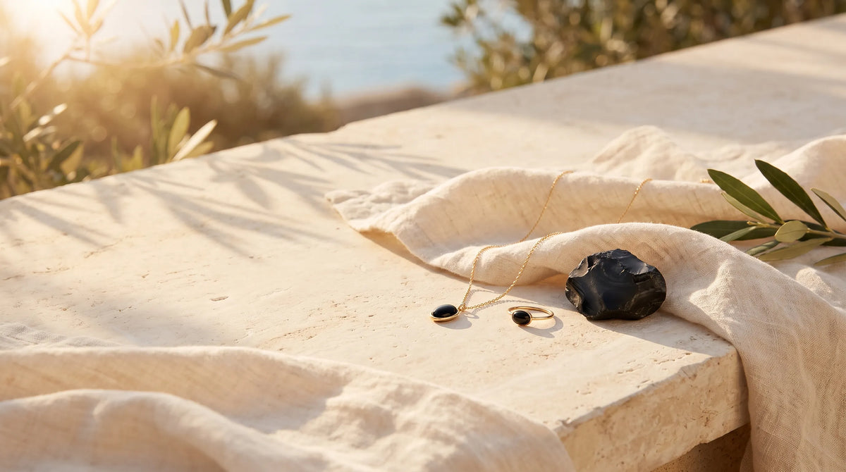 Collar y anillo de ónix negro junto a una piedra natural de ónix sobre una superficie clara con luz mediterránea. anna piedra