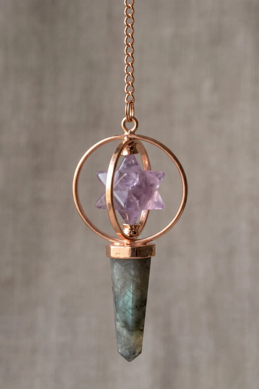 Primer plano de un péndulo Merkaba con estrella de amatista violeta, punta de labradorita y estructura de cobre.