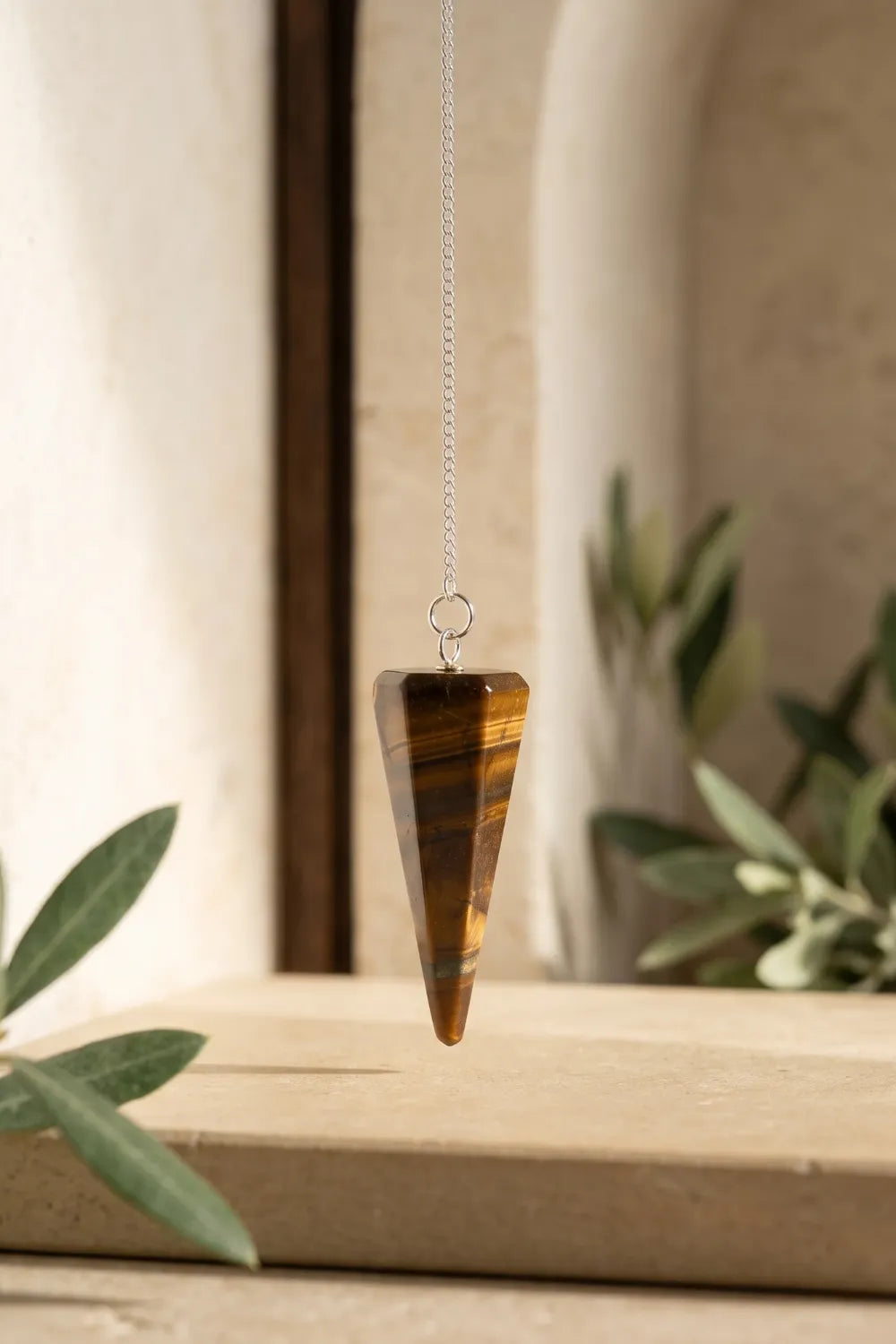 Péndulo de ojo de tigre de piedra natural suspendido verticalmente, con tonos marrones y reflejos dorados.
