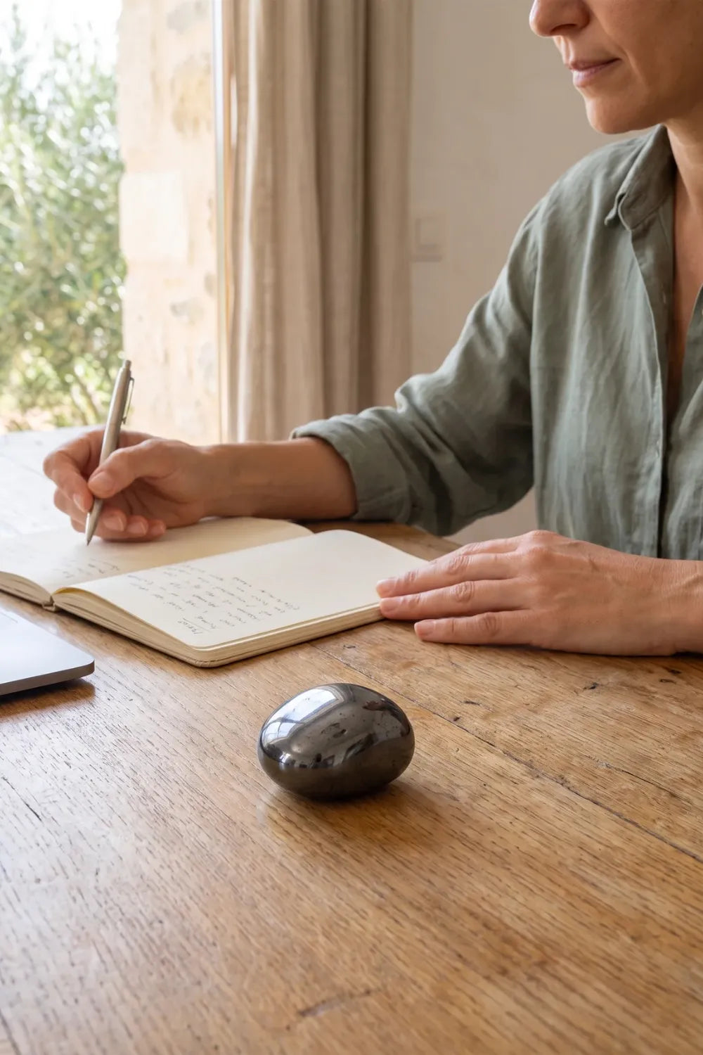 Piedra de hematita pulida sobre un escritorio de madera junto a una mujer escribiendo en un cuaderno. anna piedra