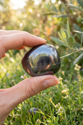 Piedra de hematita pulida sostenida entre los dedos en un jardín mediterráneo. anna piedra