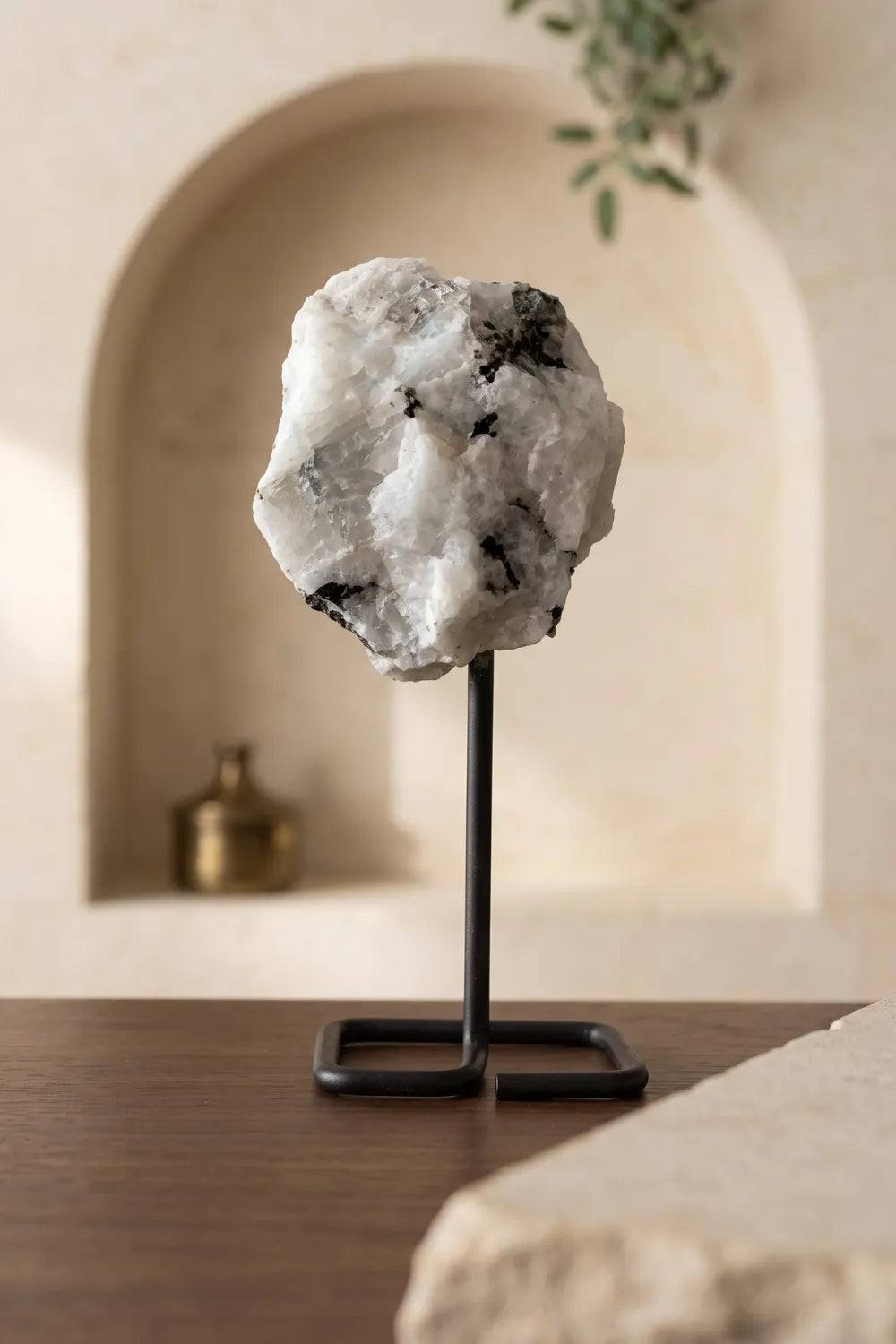 Piedra luna en bruto con soporte de metal sobre una mesa de madera, con nicho decorativo al fondo