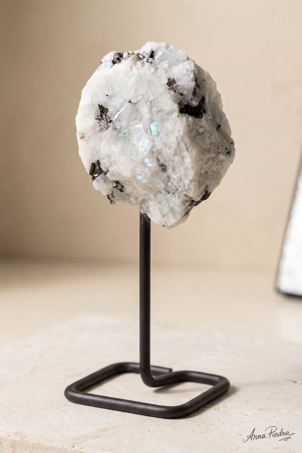 Primer plano de una piedra luna en bruto con soporte de metal sobre una superficie clara