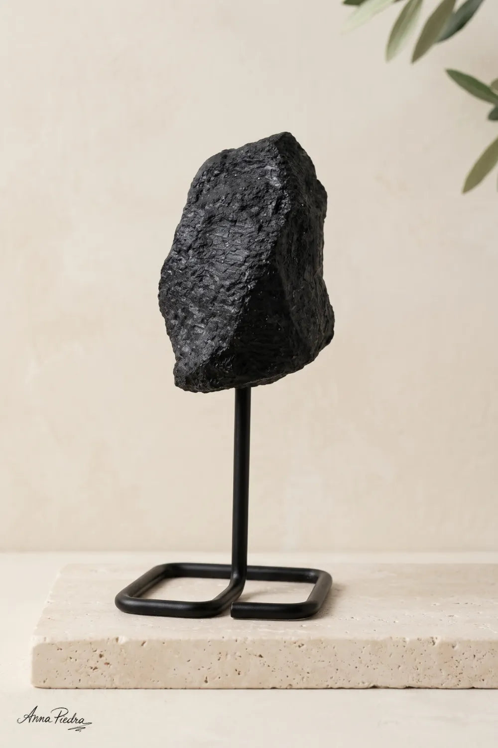 Primer plano de una piedra de turmalina negra en bruto con superficie rugosa y estriada, presentada sobre un soporte metálico negro.