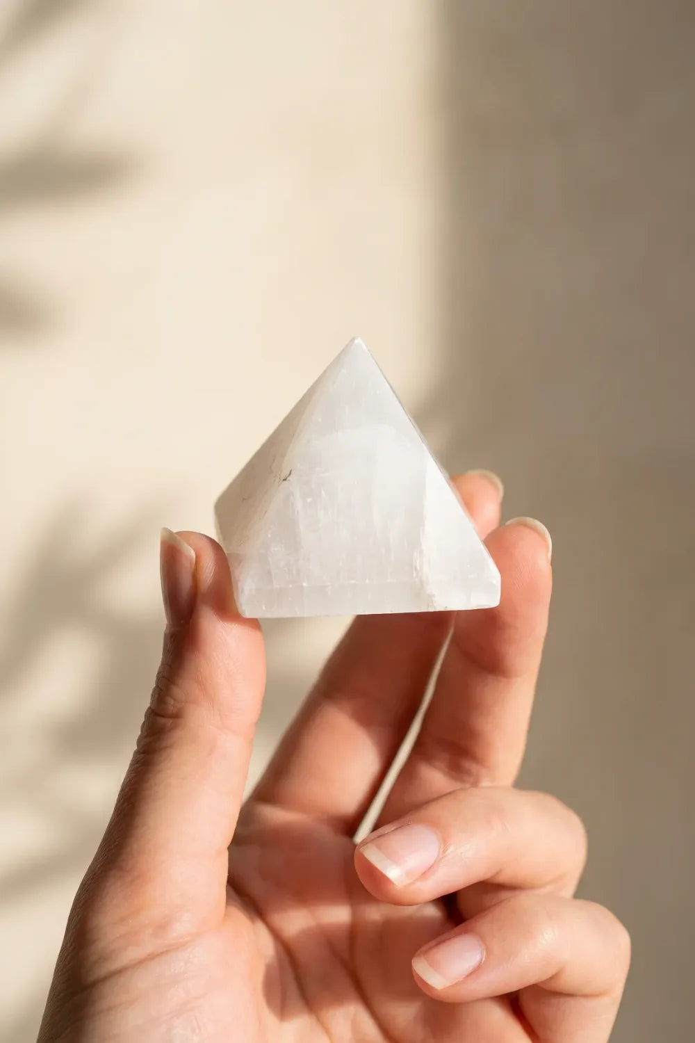 Mujer sosteniendo una pirámide de selenita natural en la mano, mostrando su textura y brillo - Anna Piedra