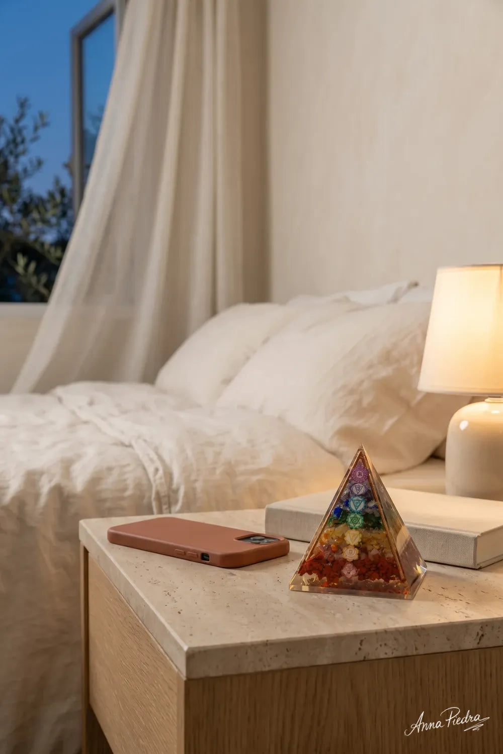 Pirámide de orgonita 7 chakras sobre una mesita de noche en un dormitorio luminoso. anna piedra