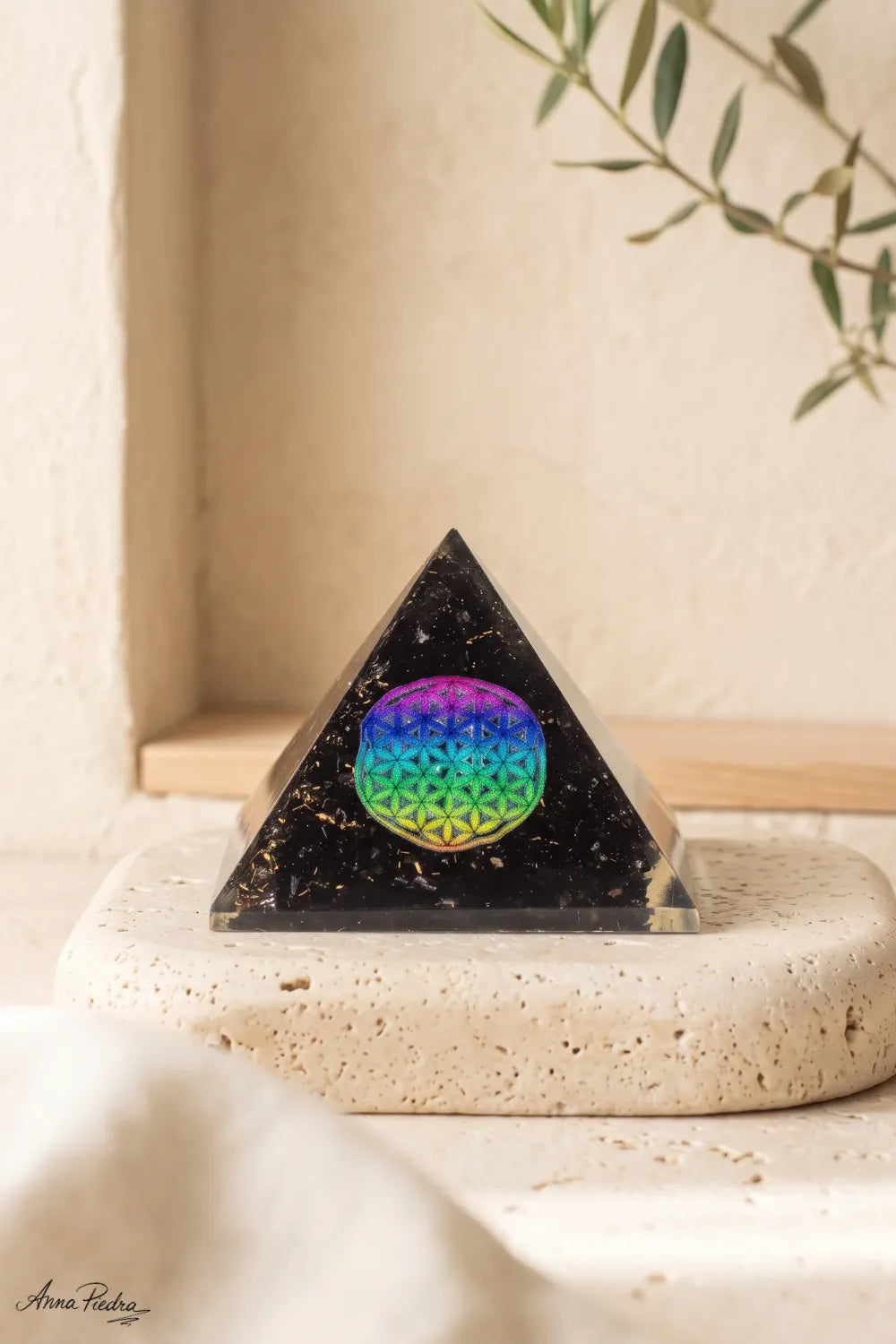 Vista frontal de pirámide de orgonita con turmalina negra, inclusiones doradas y símbolo de la Flor de la Vida multicolor.