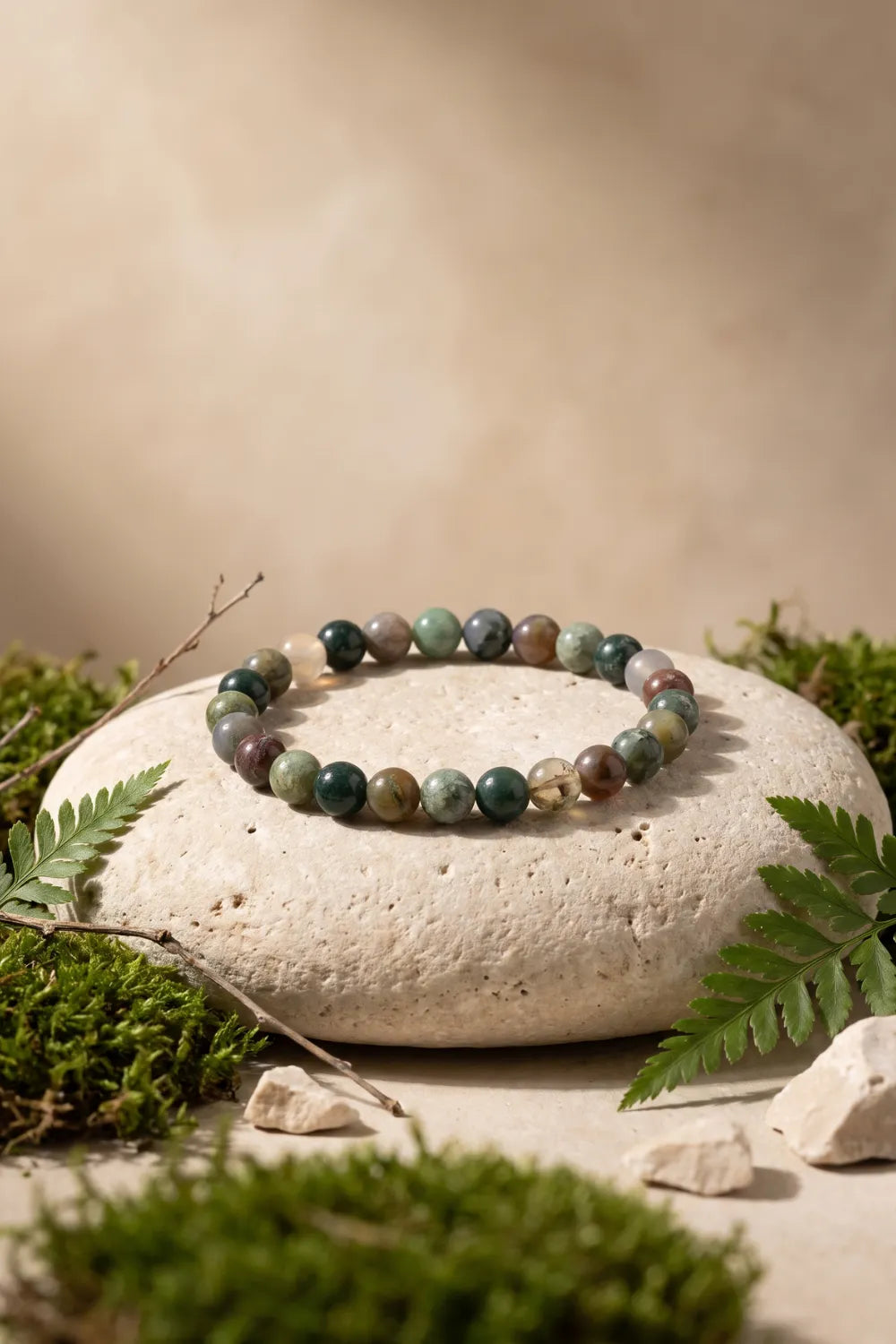 Pulsera de ágata musgosa con cuentas de piedra natural en tonos verdes y terrosos, sobre una piedra clara rodeada de musgo y helechos – Anna Piedra