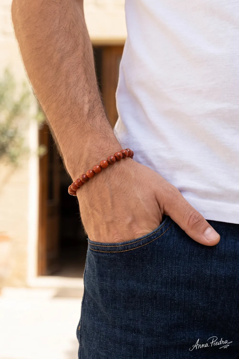 Pulsera de cornalina para hombre con cuentas redondas de piedra natural rojiza, llevada con camiseta blanca y pantalón vaquero azul – Anna Piedra
