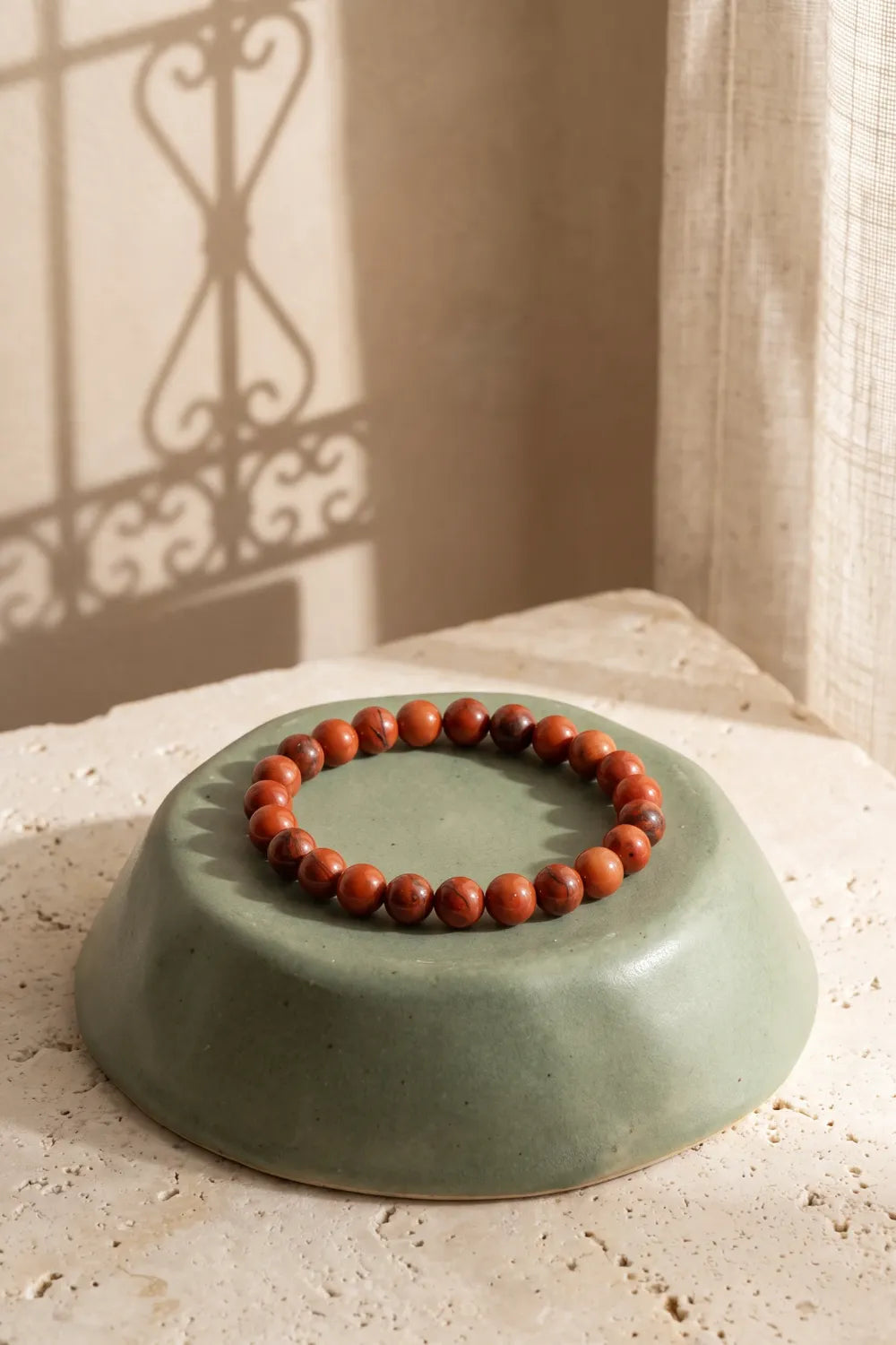 Pulsera de cornalina natural con cuentas pulidas de color rojo anaranjado y vetas oscuras, sobre un cuenco de cerámica verde salvia – Anna Piedra
