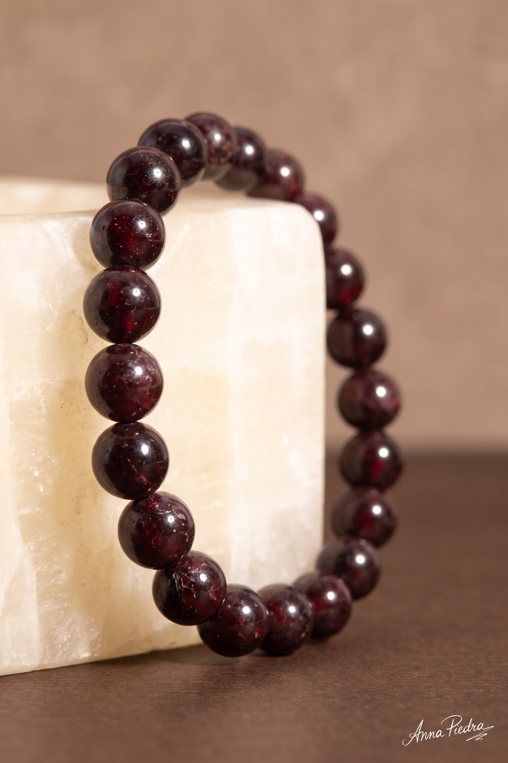 Detalle de pulsera de granate natural con cuentas redondas rojo oscuro apoyada sobre un bloque de piedra clara