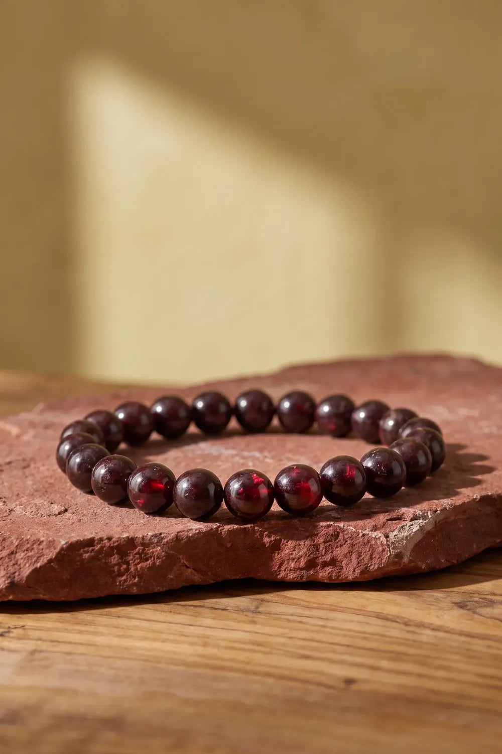 Pulsera de granate natural de cuentas pulidas color burdeos presentada sobre una piedra rojiza en una mesa de madera