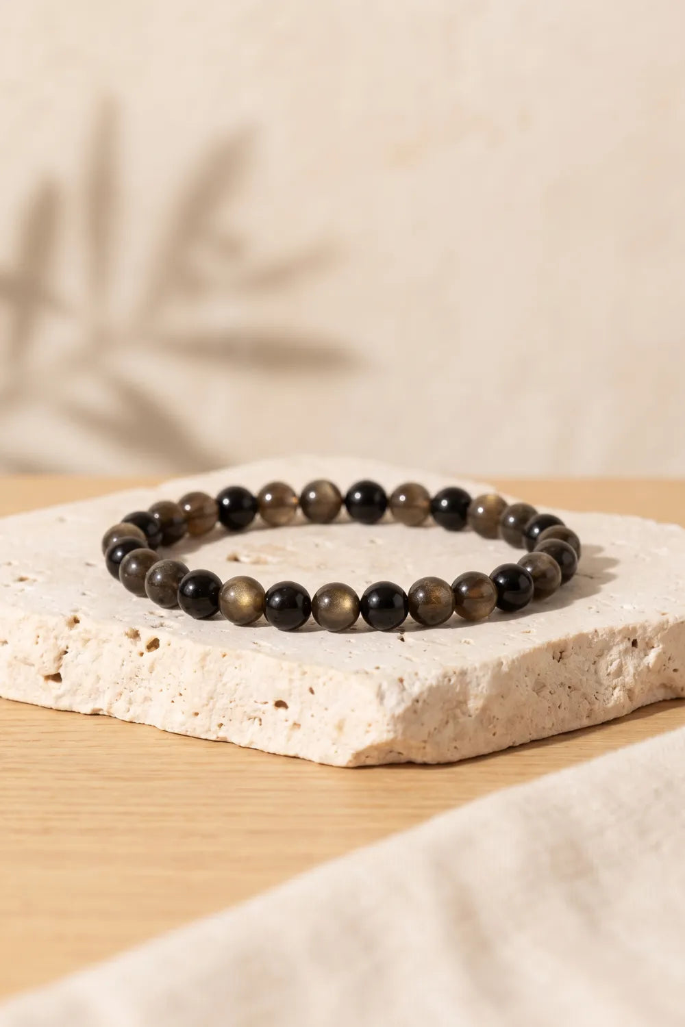 Pulsera de obsidiana dorada de cuentas redondas de 6 mm, con tonos negros y reflejos cobrizos, sobre una base de travertino – Anna Piedra