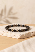 Pulsera de obsidiana dorada de cuentas redondas de 6 mm, con tonos negros y reflejos cobrizos, sobre una base de travertino – Anna Piedra