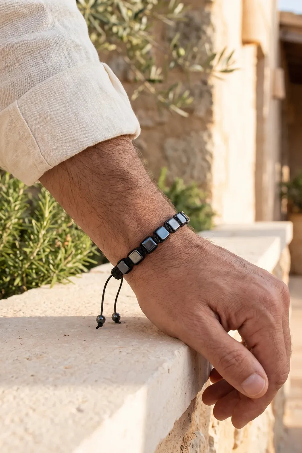 Detalle de una pulsera de hematita ajustable en la muñeca de un hombre en un entorno mediterráneo. anna piedra
