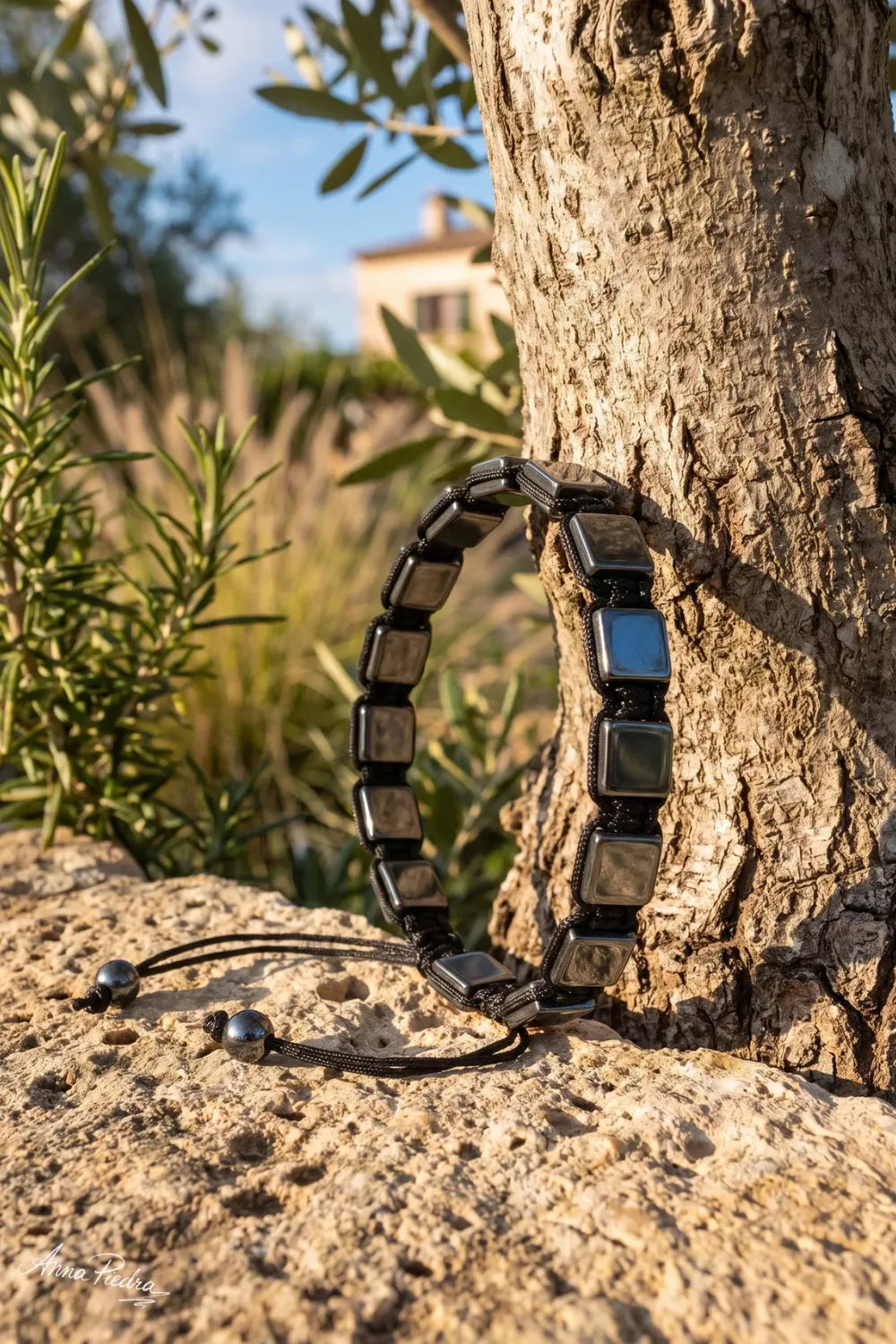 Pulsera de hematita shamballa para hombre apoyada junto a un olivo sobre piedra natural. anna piedra