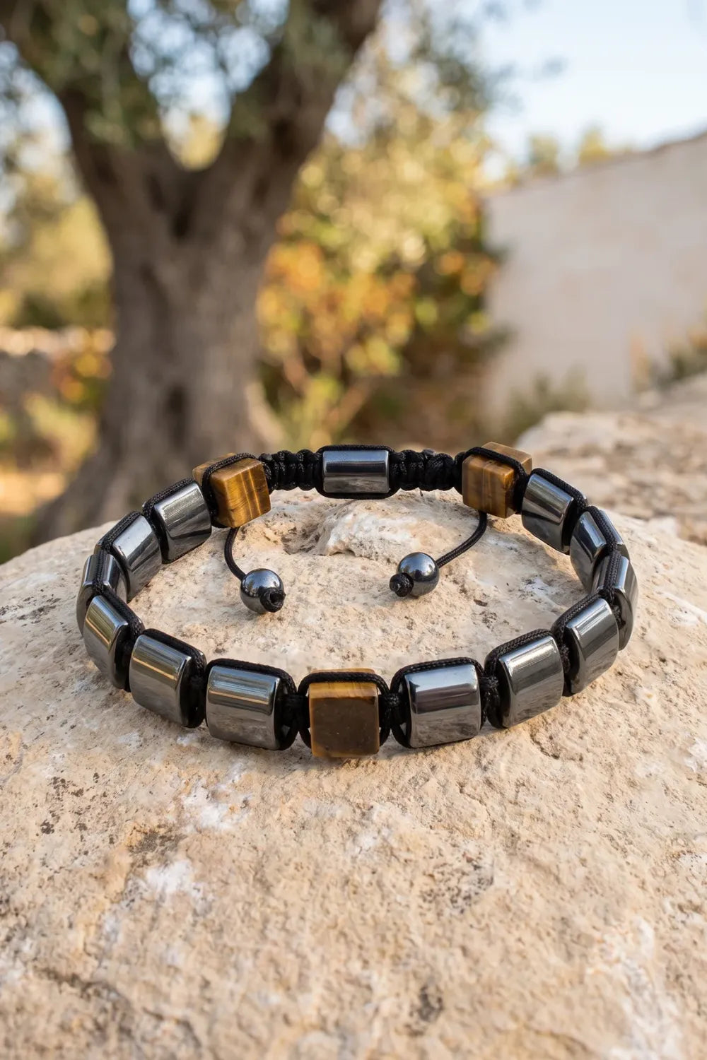 Pulsera de hematita y ojo de tigre con cierre shamballa ajustable apoyada sobre piedra natural en un entorno mediterráneo. anna piedra