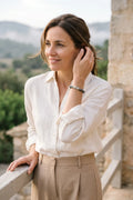 Mujer con camisa blanca llevando una pulsera de jade de montaña y hematita en un mirador de estilo mediterráneo.