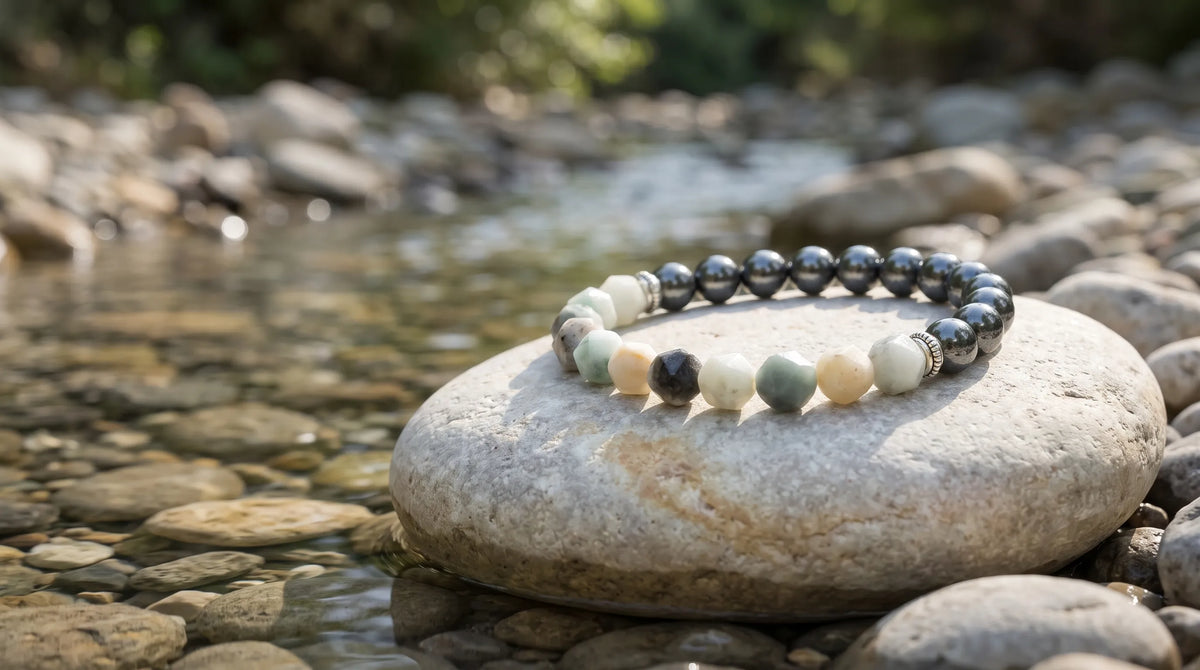 Pulsera de jade de montaña y hematita colocada sobre una piedra lisa junto a un arroyo de agua clara.