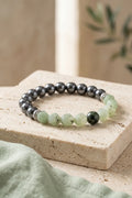Pulsera de piedras naturales con cuentas de jade verde facetado y hematita gris metalizada sobre una base de piedra beige.