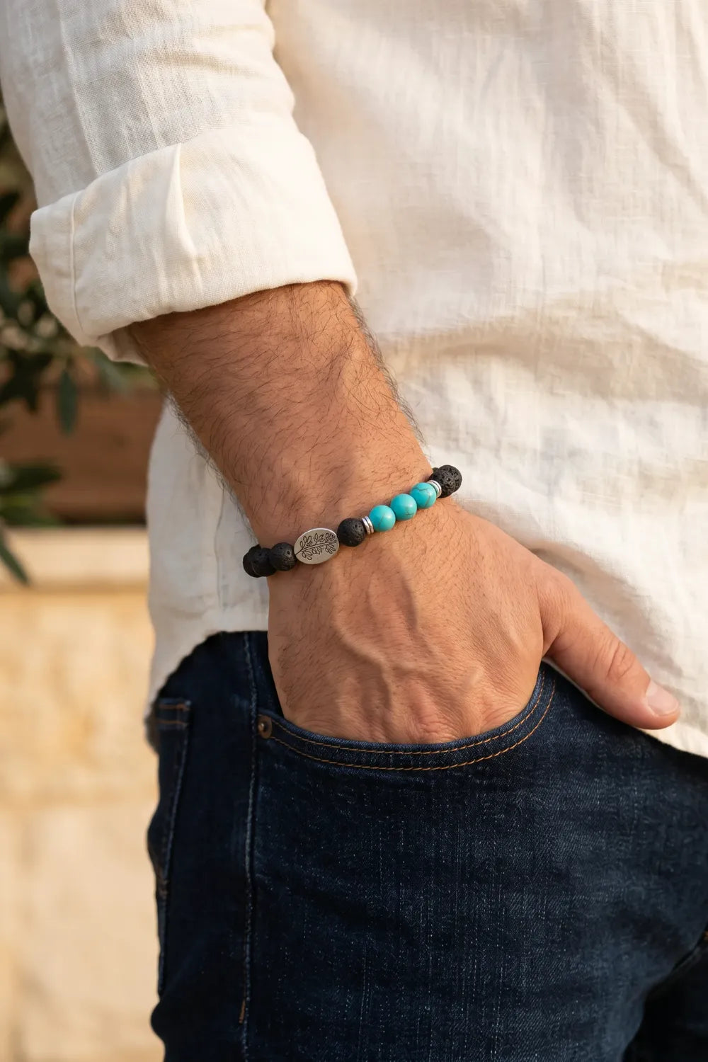 Primer plano de la muñeca de un hombre con una pulsera de lava y turquesa combinada con camisa blanca y vaqueros.