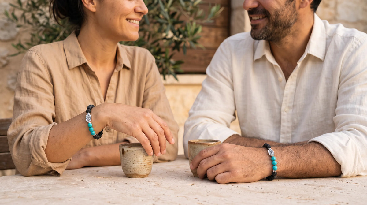 Hombre y mujer sentados a la mesa con tazas de café, ambos llevando una pulsera de lava y turquesa.
