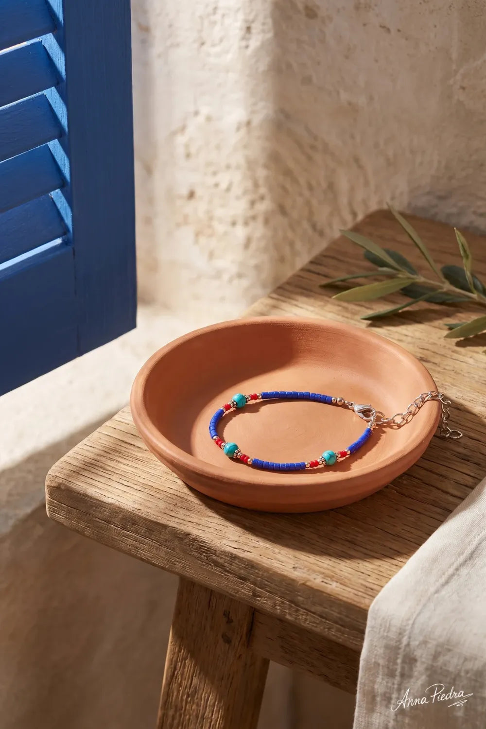 Pulsera nepalí de ónix azul colocada en un plato de barro sobre una mesa de madera junto a una ventana azul anna piedra