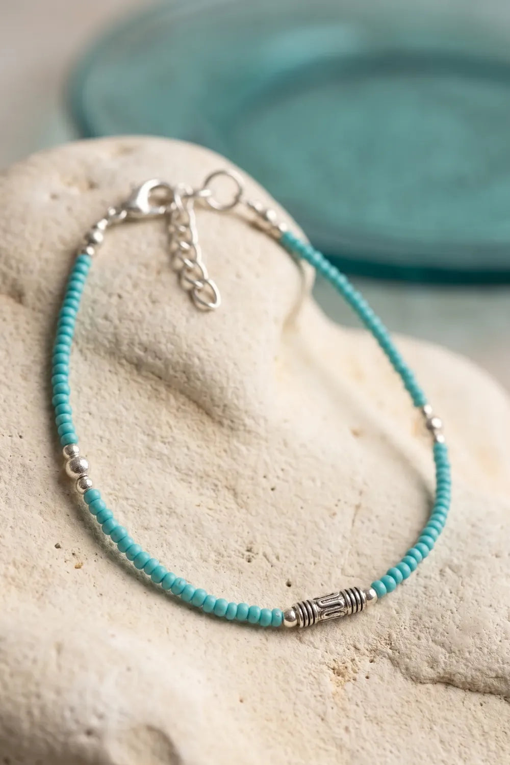 Primer plano de una pulsera de turquesa azul con cuentas pequeñas, adornos plateados y cadena de extensión.
