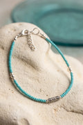 Primer plano de una pulsera de turquesa azul con cuentas pequeñas, adornos plateados y cadena de extensión.